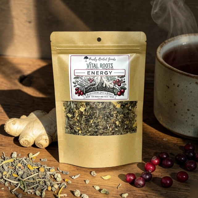 vital roots energy tea sitting on wooden counter with berries, herbs, ginger, and a cup of warm tea

